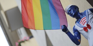 Eine Regenbogenfahne hängt neben einer Matrosenfigur