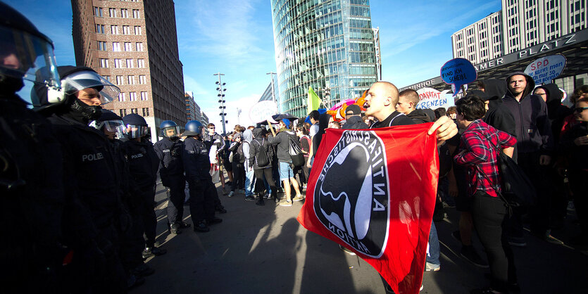 Polizei und Demonstranten vor Hochhäusern und blauem Himmel