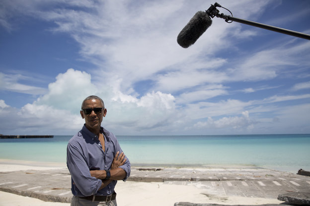 Obama steht vor dem Meer; im rechten Bildrand ragt ein Mikrofon ins Bild.