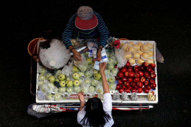 Vogelperspektive: Ein Mann verkauft Obst an eine Frau.