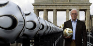 Franz Beckenbauer steht vorm Brandenburger Tor mit vielen Bällen