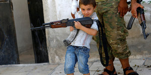 Ein Junge posiert mit einem Gewehr vor einem Kämpfer der Freien Syrischen Armee (FSA).