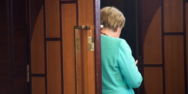 Angela Merkel steht mit dem Rücken zum Fotografen an der Tür eines Besprechungsraums in Hangzhou und schaut auf ihr Smartphone
