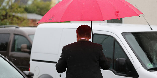 Ein Mann mit rotem Schirm läuft zwischen Autos