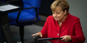 Angela Merkel steht an einem Rednerinnenpult und bläst die Backen auf