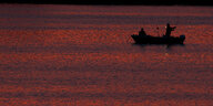 Auf dem Wasser schwimmt ein Boot mit Anglern in abendrotes Licht getaucht