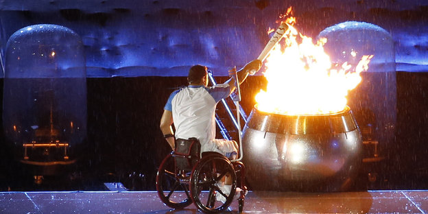Ein Mann im Rollstuhl entzündet eine Fackel an einem großen Feuer
