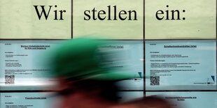 Stellenanzeigen mit der Überschrift "Wir stellen ein" hängen im Fenster einer Zeitarbeitsfirma und eine Person läuft vorbei