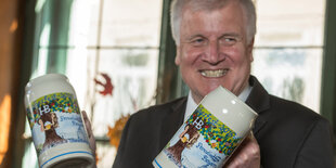 Horst Seehofer hält zwei bunte Bierkrüge