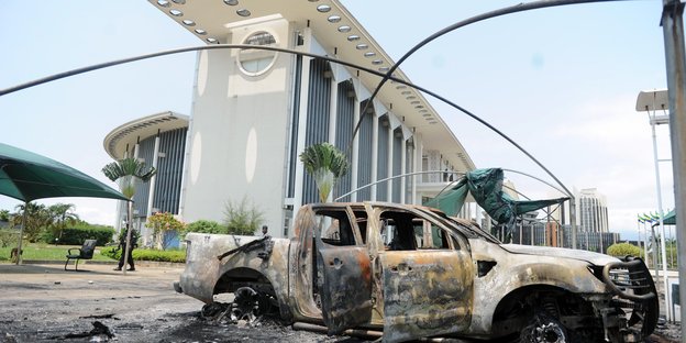 Ein ausgebranntes Auto steht vor einem hohen weißen Gebäude