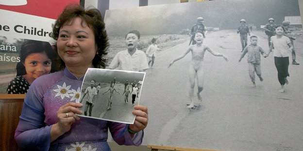 Eine Frau steht neben einem Foto, das ein vor Napalm fliehendes nacktes Mädchen im Vitenamkrieg zeigt
