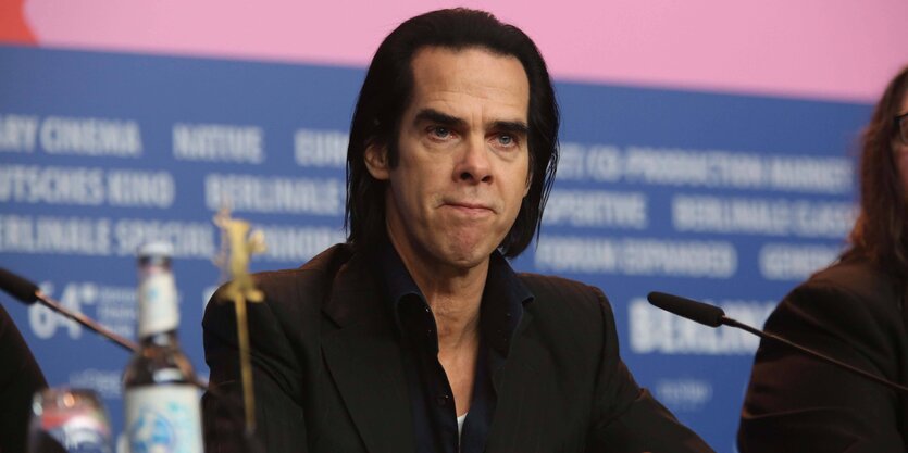 Nick Cave sitzt vor mehreren Mikrofonen