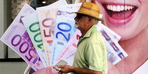 Ein älterer Mann mit Hut geht an einem großen Plakat vorbei, auf dem jemand mehrere Geldscheine lachend in der Hand hält