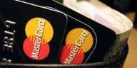 Zwei schwarze Mastercard-Kreditkarten mit rot-gelbem Logo stecken in einem Becher