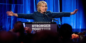 Hillary Clinton mit ausgebreiteten Armen hinter einem Rednerpult