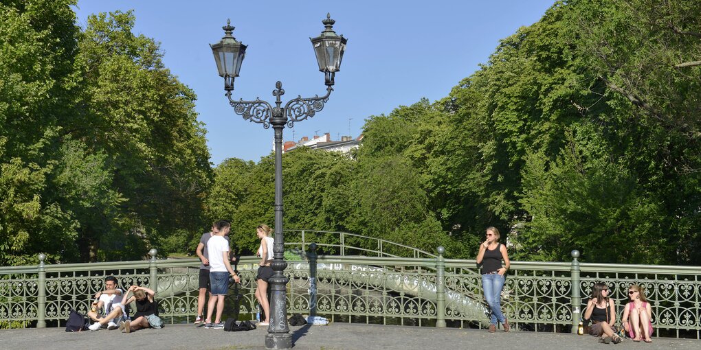 Menschen lehnen oder sitzen am Brückengeländer und genießen das schöne Wetter