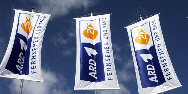 Werbefahnen von ARD und ZDF wehen vor blauem Himmel