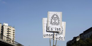 Vor blauem Himmel: Schilder mit der Aufschrift „Es ist unsere Stadt“, Häuserzeilen rechts und links am Rand