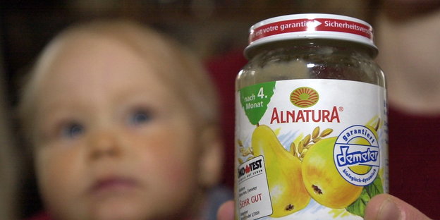Ein Glas mit Babynahrung von Alnatura, im Hintergrund das Gesicht eines Kleinkinds
