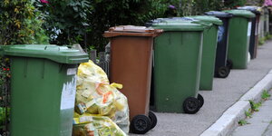 Mülltonnen und gelbe Säcke stehen auf einem Gehweg