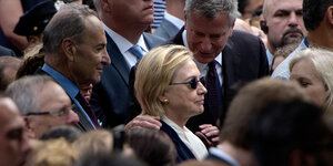 Hillary Clinton trägt eine schwarze Sonnenbrille und steht in einer Menschenmenge