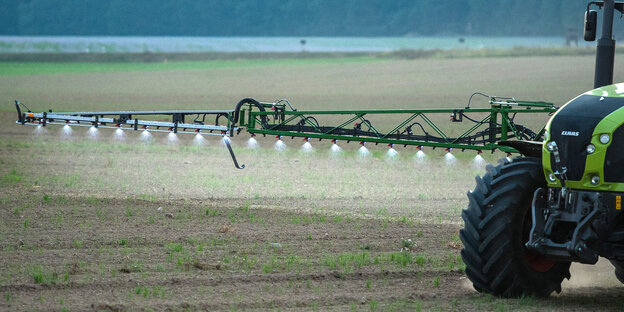 Ein Traktor fährt über ein Feld und versprüht über viele Düsen Pestizid
