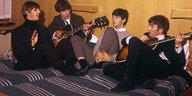 Vier Männer (die Beatles) mit Gitarren auf einem Hotelbett