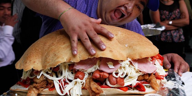 Dicker Mann drückt riesigen Sandwich voller Fleisch zusammen