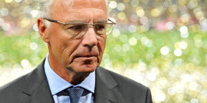 Beckenbauer guckt ernst, hinter im ist unscharf glitzerner Regen zu erkennen