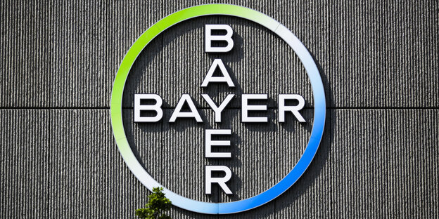 Vor dem Logo auf einer Wand der Firma Bayer wächst ein Baum
