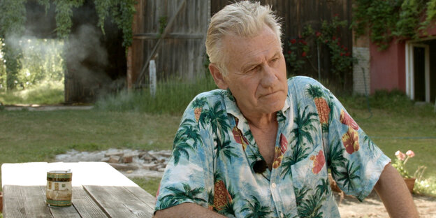 Alter Mann im Hawaiihemd sitzt im Freien an einem Tisch