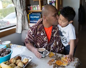 Ein Mann sitzt am Küchentisch und küsst seinen Sohn auf die Wange