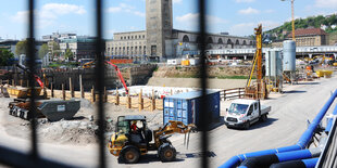 Durch Gitter blickt man auf eine Baustelle, auf der ein Bagger fährt