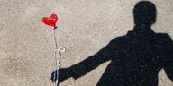 Ein roter Herzluftbalon ohne Luft liegt auf dem Boden. Dazu der Schatten eines Menschen, so fotografiert, als hielte er den Balon fest