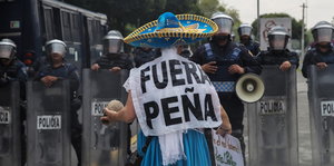 Eine Demonstrantin mit Anti-Peña-Plakat steht vor Polizisten