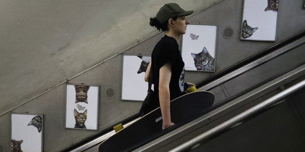 Eine Frau fährt die Rolltreppen nach oben. Hinter ihr auf den Werbeplakatensind Katzenbilder zu sehen