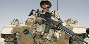 Soldat steht mit G36 im Arm vor einem Panzer