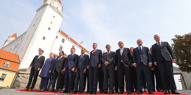 viele Männer und wenige Frauen stehen für ein Foto auf einem roten Teppich vor einer Burg