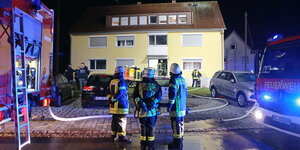 Feuerwehrmänner stehen vor einem Haus, links und rechts im Bild sind Feuerwehrfahrzeuge zu sehen