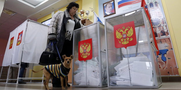 Eine Frau mit Hund an der Leine wirft ihren Wahlzettel in eine Wahlurne