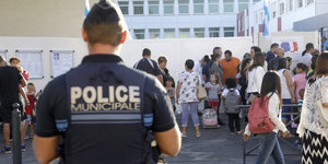 Kinder und Erwachsene vor dem Eingang einer Schule, im Vordergrund ein Polizist mit dem Rücken zur Kamera