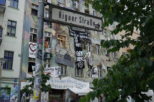 Ein Straßenschild der Rigaer Straße mit einer Hausfassade im Hintergrund