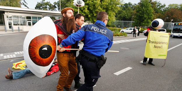 Ein Mann rangelt mit einem Polizisten um ein Pappmasché-Auge, das an einer Stange befestigt ist