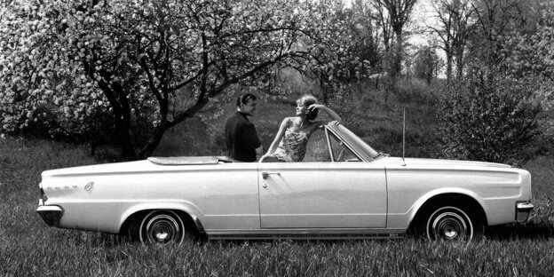 Ein Mann und eine Frau sitzen in einem Cabrio. Der Wagen steht vor einem blühenden Obstbaum