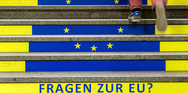 Ein Manh geht eine Treppe hoch, auf der die Europaflagge und die Aufschrift "Fragen zur EU?" zu sehen sind