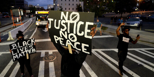 Menschen mit Protestschildern, in der Bildmitte mit der Aufschrift „No justice no peace“
