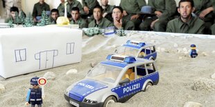 Uniformierte sitzen an einem Sandkasten mit Spielzeugfiguren