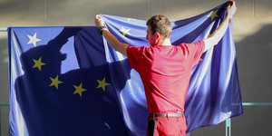 Ein Mann hängt Europaflagge über ein Geländer