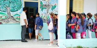 Viele Kinder stehen in der Reihe aufgestellt vor einem Schuleingang. Die Fassade der Schule ist bunt bemalt