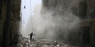 Ein Mann balanciert, umhüllt von einer Wolke aus Staub, über die Trümmer auf den Straßen Aleppos